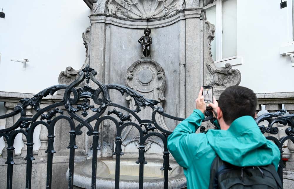 Un uomo con impermeabile e zaino, di spalle mentre scatta una foto al Manneken Pis, nel centro storico di Bruxelles