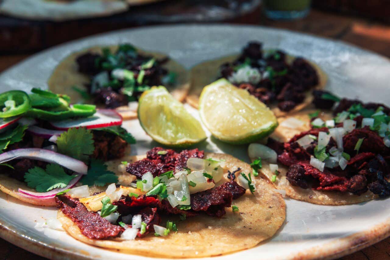 Um prato branco com tacos al pastor e limão