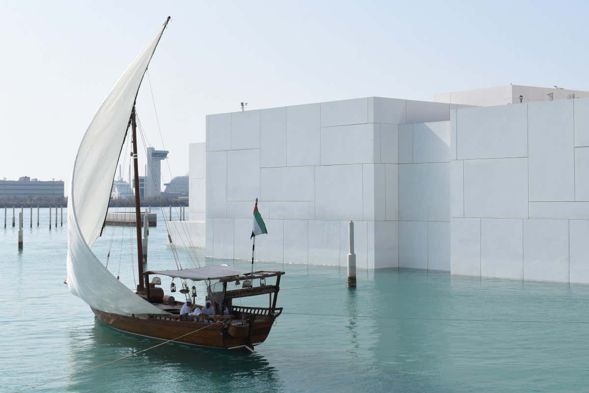 Un barco de vela tradicional árabe navegando frente a un vanguardista edificio