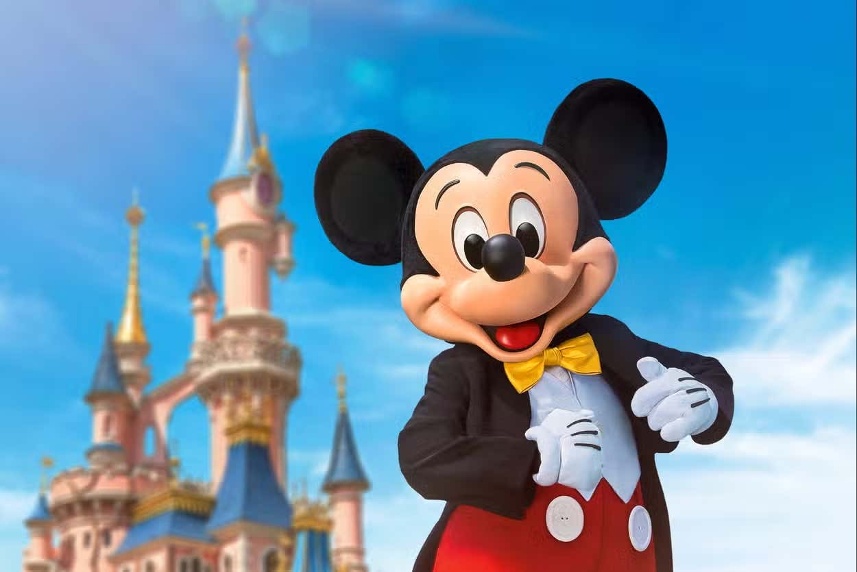 Primer plano con Mickey Mouse con el castillo de Disneyland Paris de fondo y el cielo azul