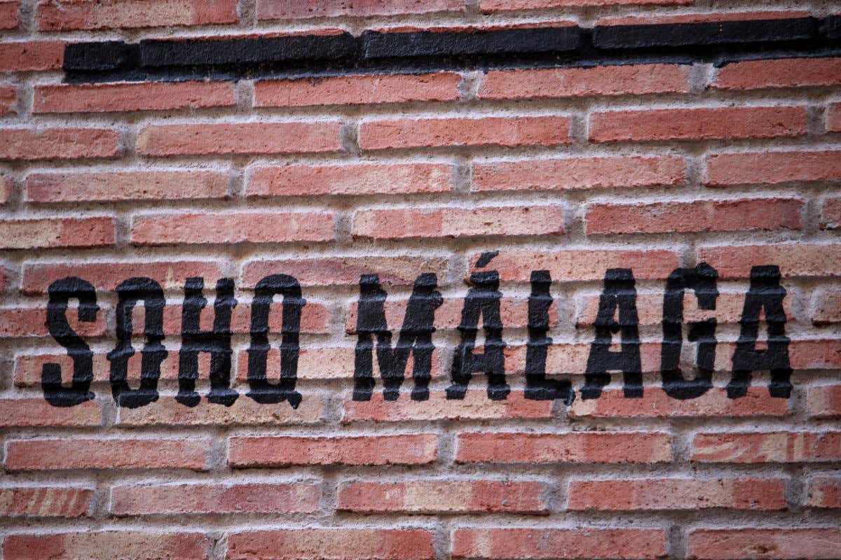 Un muro de ladrillos rojizos con unas letras pintadas en negro indicando Soho Málaga
