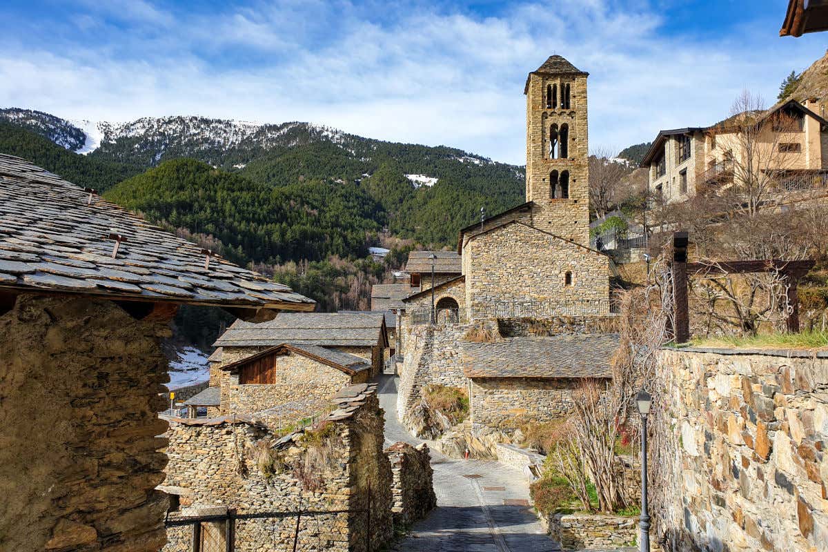 Una calle con casas de piedra y una iglesia románica frente a una cima montañosa con algo de nieve