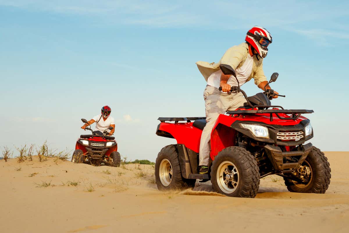 Dos hombres en quads rojos, cada uno de ellos en un vehículo, recorriendo un paraje desértico
