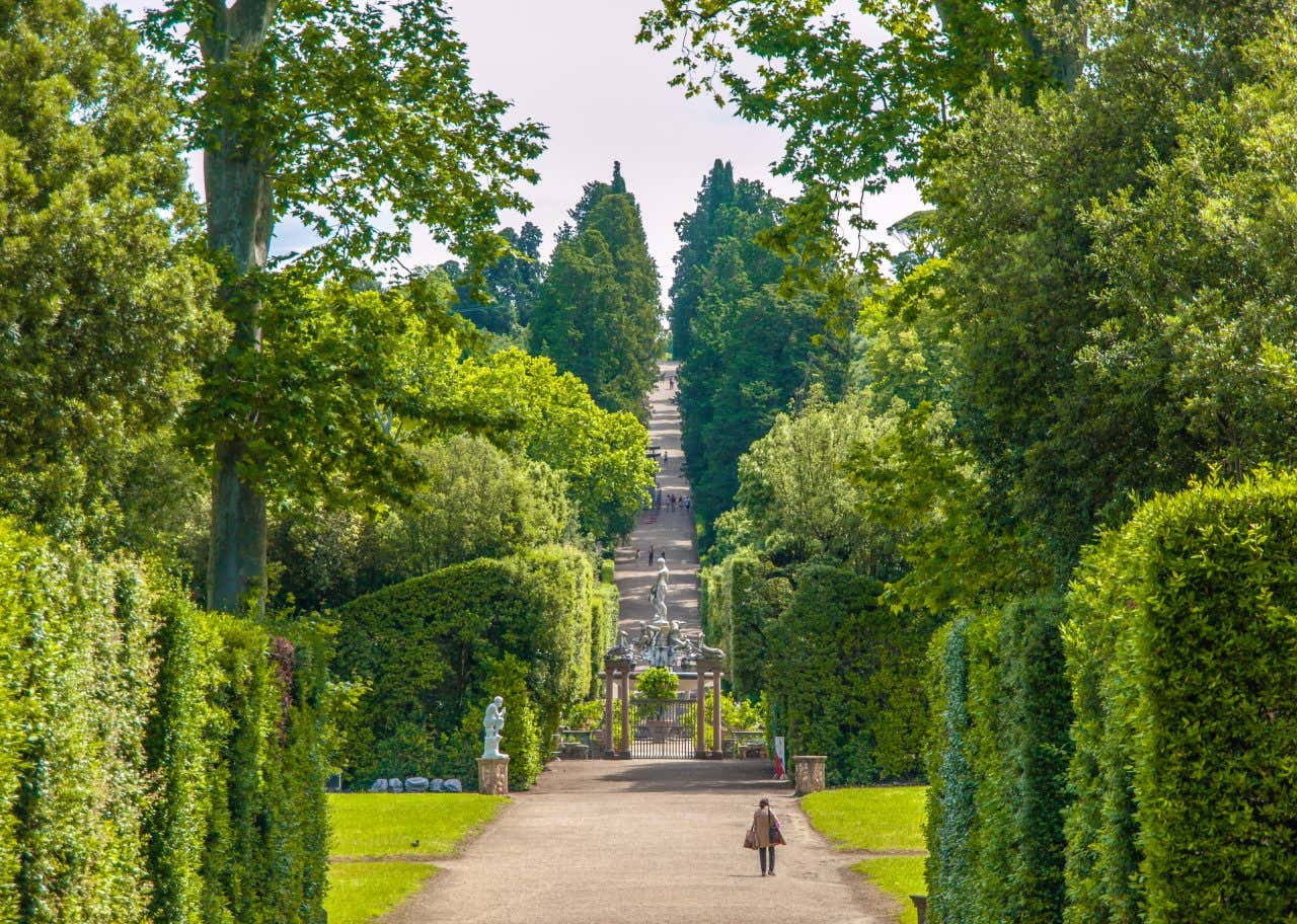 A large park with green vegetation, statues, and a fountain in the distance on a sunny day