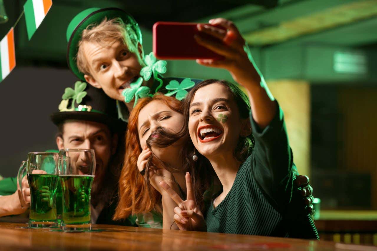 Due ragazze e due ragazzi si scattano una foto al bancone di un pub con davanti due pinte di birra verde