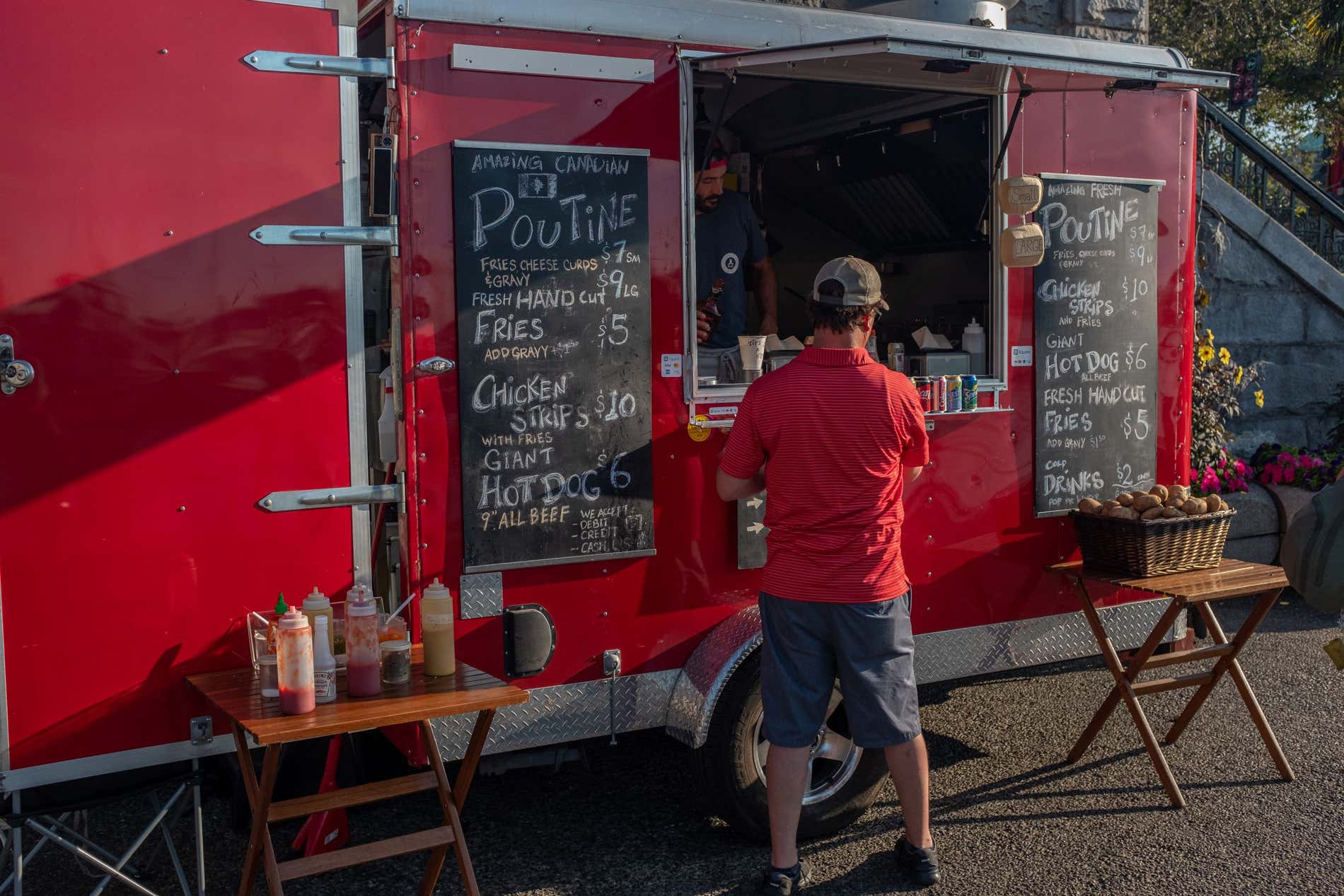 Un uomo che ordina del cibo a un camioncino, con due cartelli di gesso sul camioncino, con poutine scritto in grande