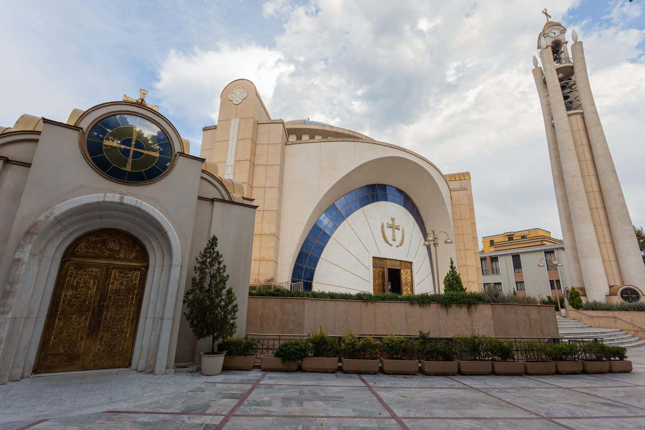 La facciata esterna e opulenta di una chiesa moderna, con campanile, edificio principale decorato con vetrate e dalla particolare forma circolare, e un terzo edificio più piccolo laterale