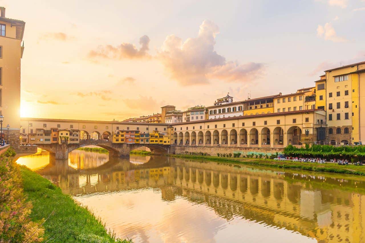 A stone bridge with shops over a river in Florence at sunset