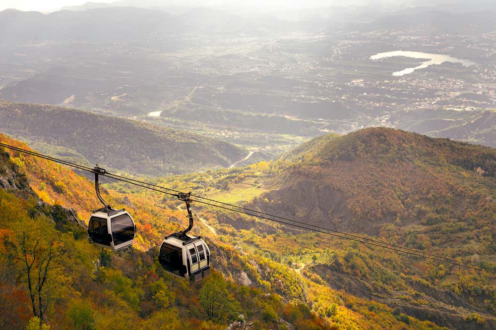 Due cabine della funicolare che porta in cima al monte Dajt con il bosco sottostante che sfoggia dei brillanti colori autunnali