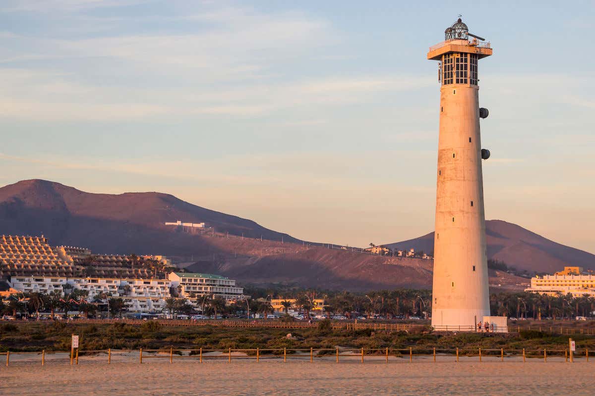 Un faro de grandes disensiones emplazado en la arena y con varias montañas al fondo
