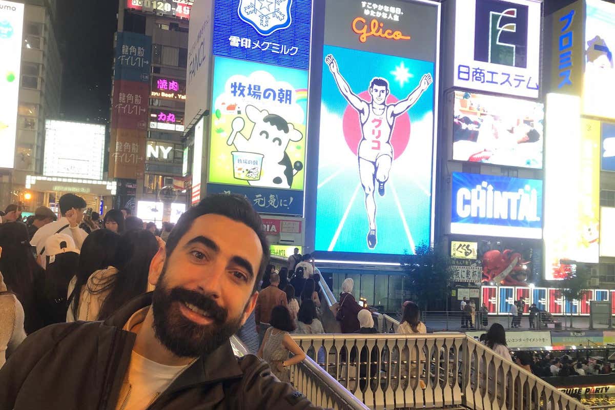 Imagen nocturna de un hombre frente al letrero de Glico en Osaka, Japón