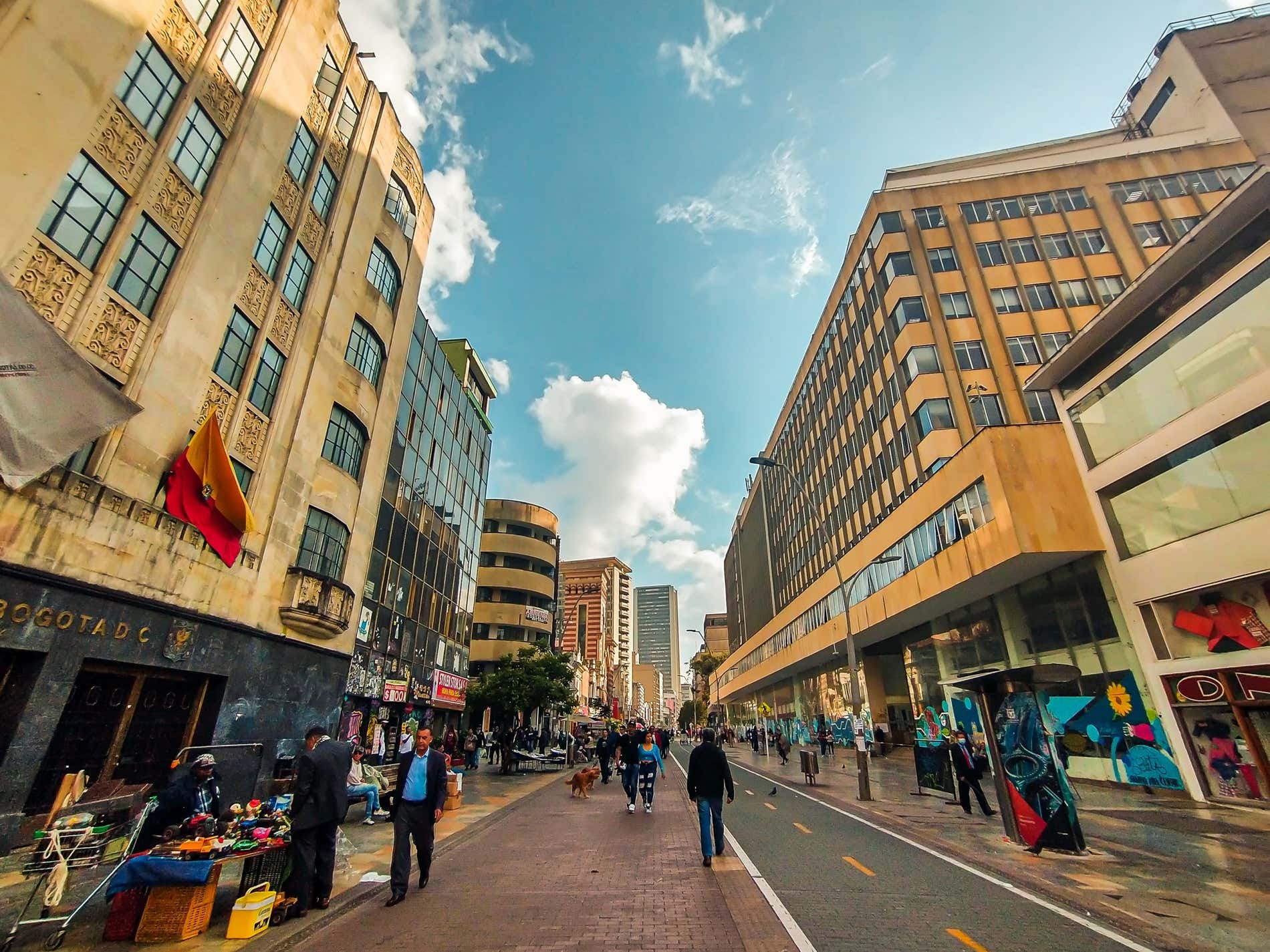 Una calle en Bogotá, Colombia, con gente caminando, y un cielo azul nublado al fondo