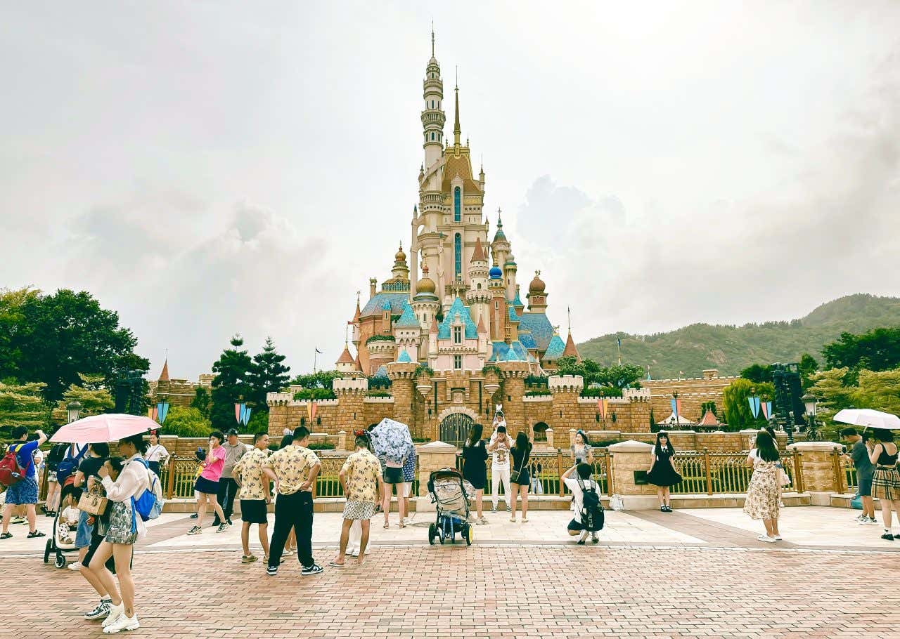 Disney Castle, Disneyland Hong Kong on a cloudy day, with lots of travelers taking photographs.