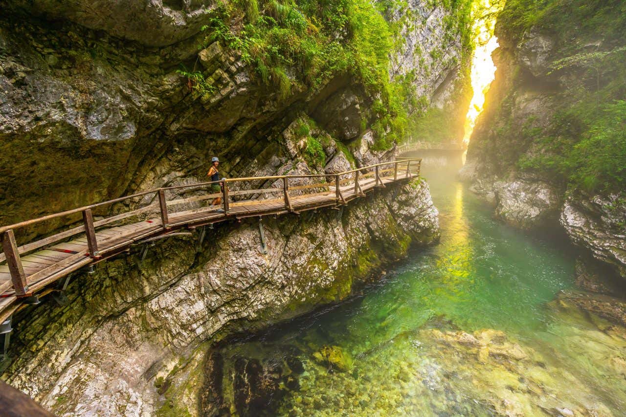Una donna percorre una passerella di legno all'interno di una gola naturale in cui scorre un fiume