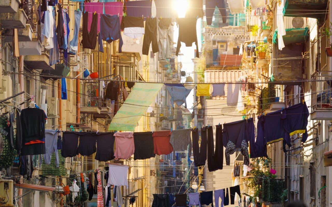 Panni stesi tra i balconi di un vicolo napoletano con edifici storici sullo sfondo