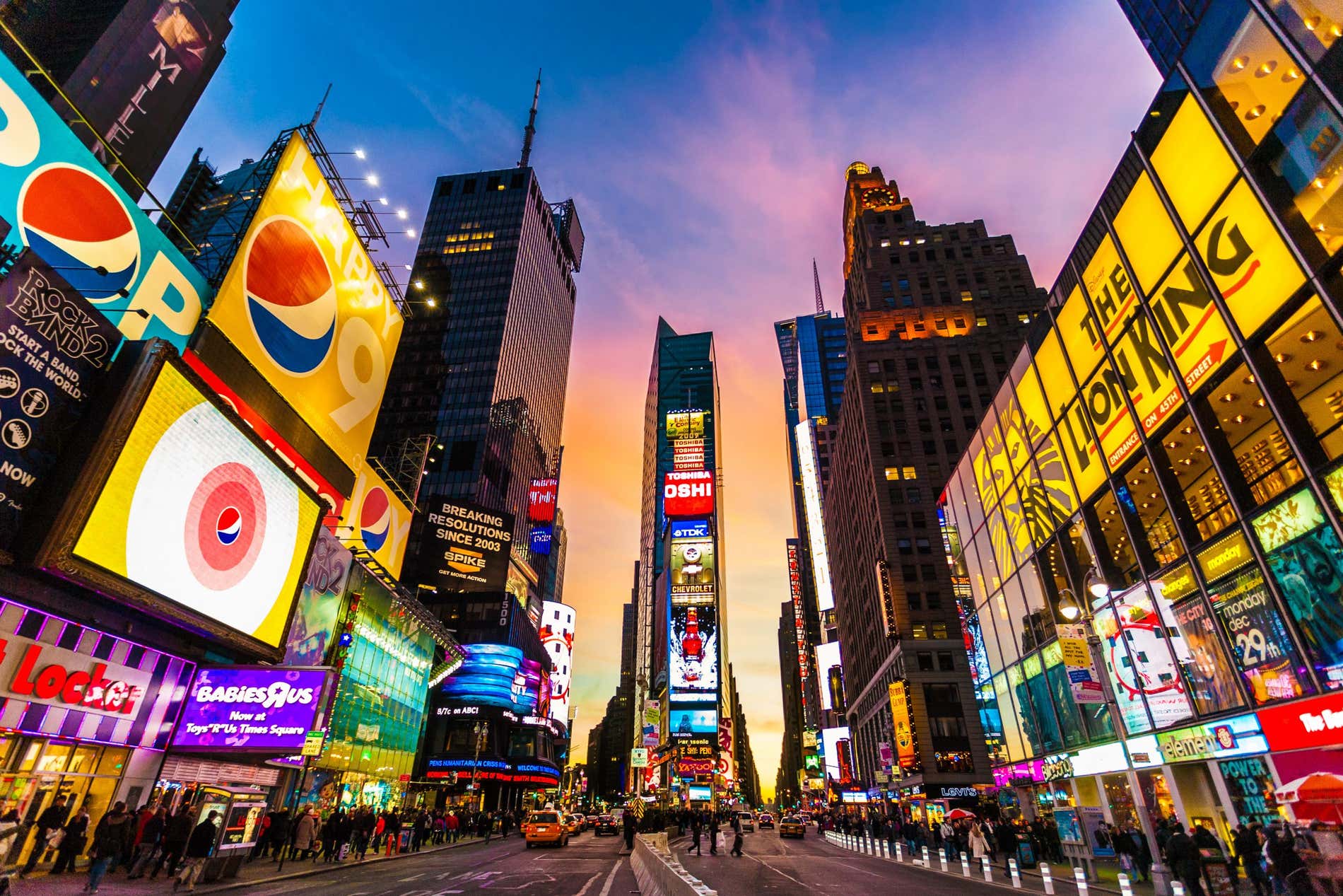 Times Square illuminata di sera, con un cielo viola e arancione sullo sfondo
