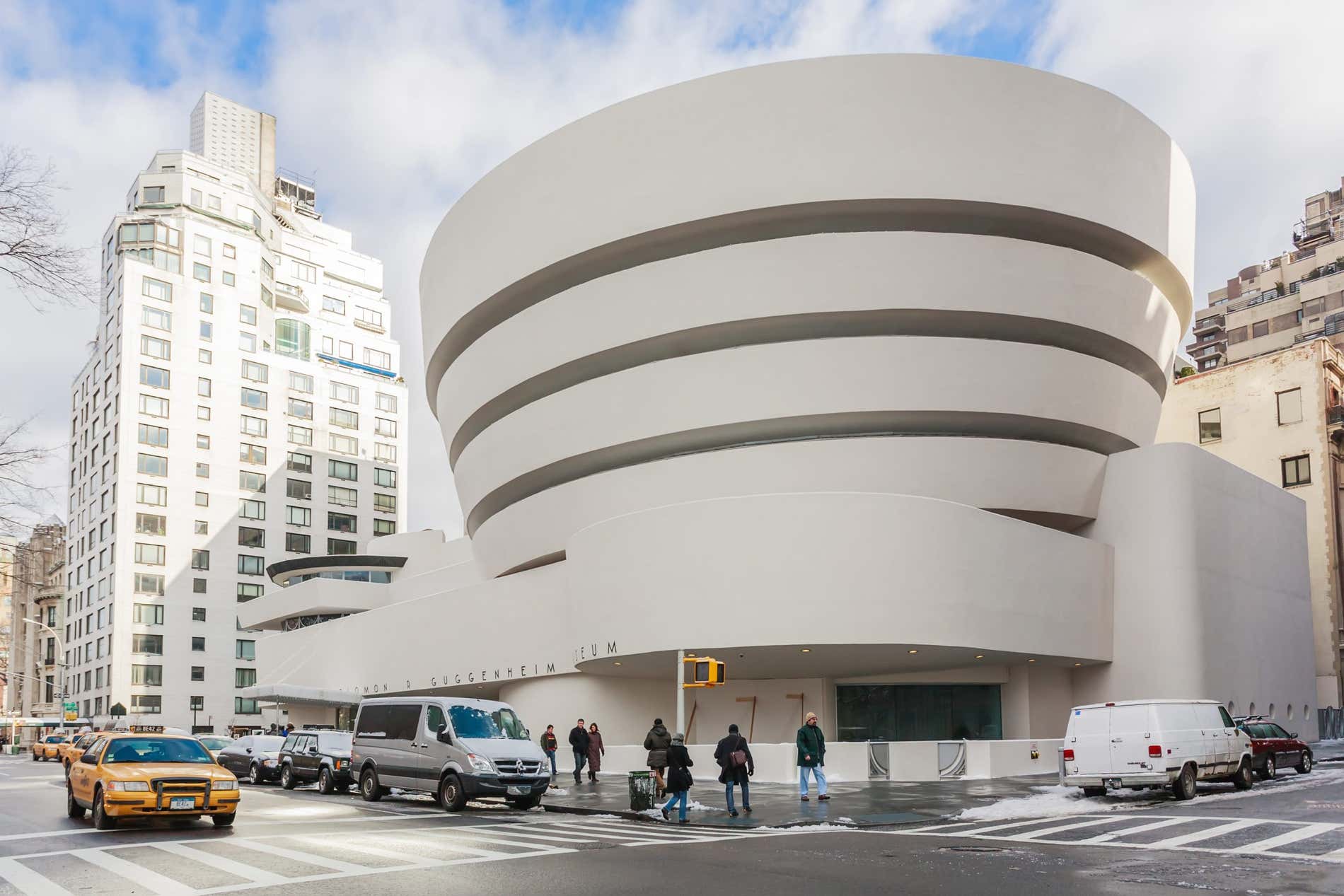 Il bianco brillante del Guggenheim Museum di New York visto dall'altra parte della strada, con un taxi che sfreccia sulla carreggiata e auto parcheggiate lungo il viale