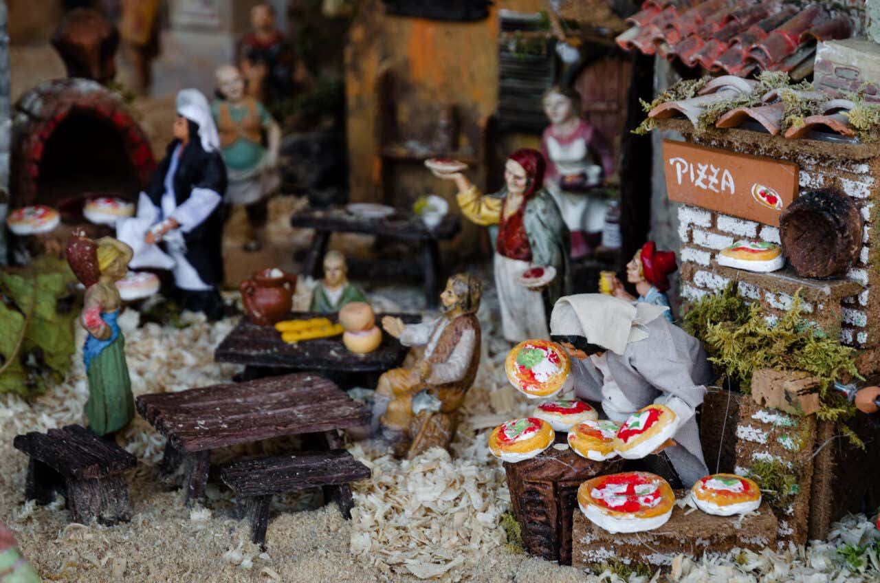 Statuine di un presepe ritratte nell'atto di sfornare e mangiare delle pizze da un forno in pietra