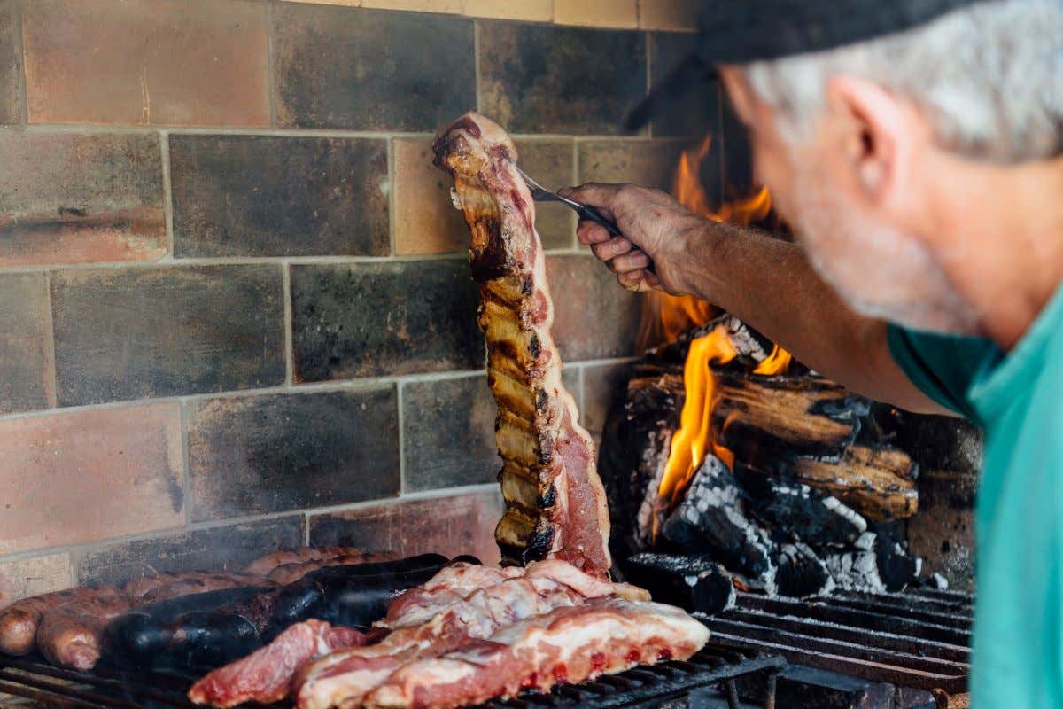 Un hombre frente a un asador moviendo unos cortes de carne