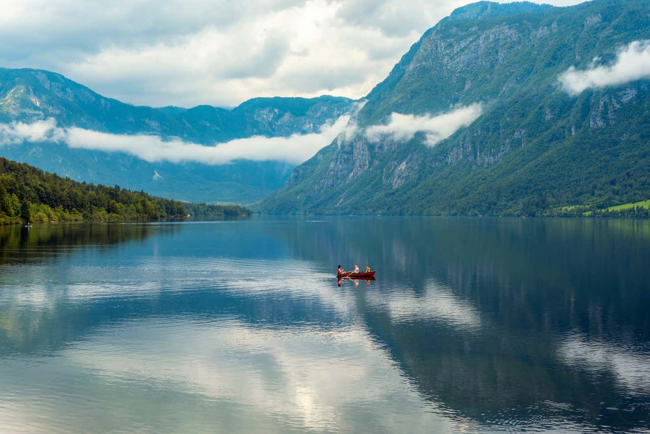 Una barca roja en mitad del lago Bohinj, en Eslovenia, un día nublado