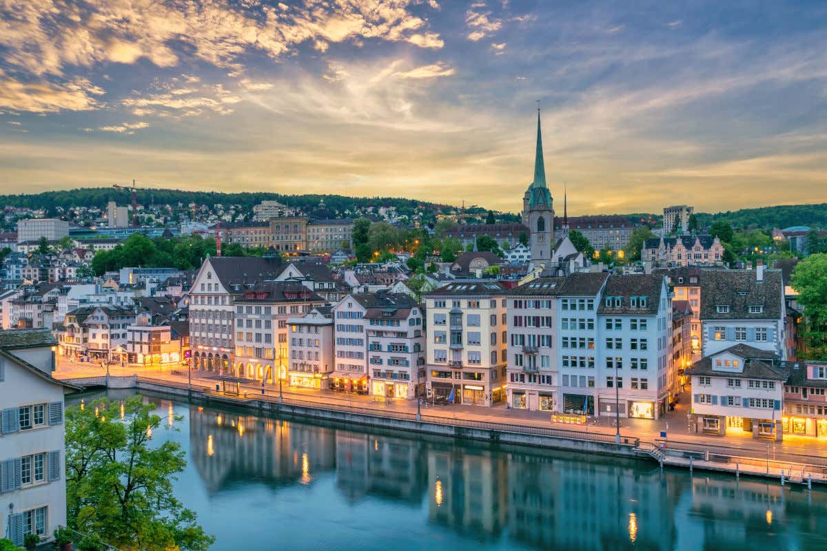 Varias casas alrededores de un canal de Zúrich al atardecer con las farolas iluminadas