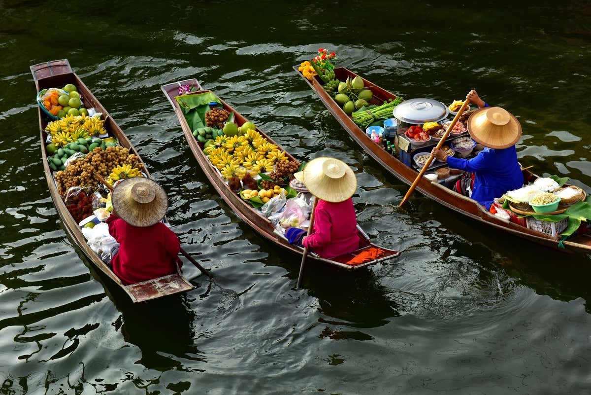 Tres vendedores a bordo de tres barcas con productos en el mercado flotante de Damnoen Saduak