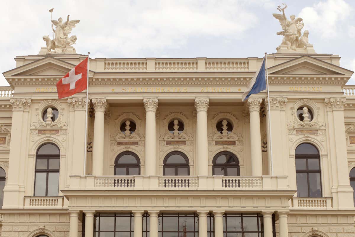 Edificio de la Ópera de Zúrich, que destaca por su fachada blanca decorada con algunos bustos y columnas, así como por la bandera de Suiza