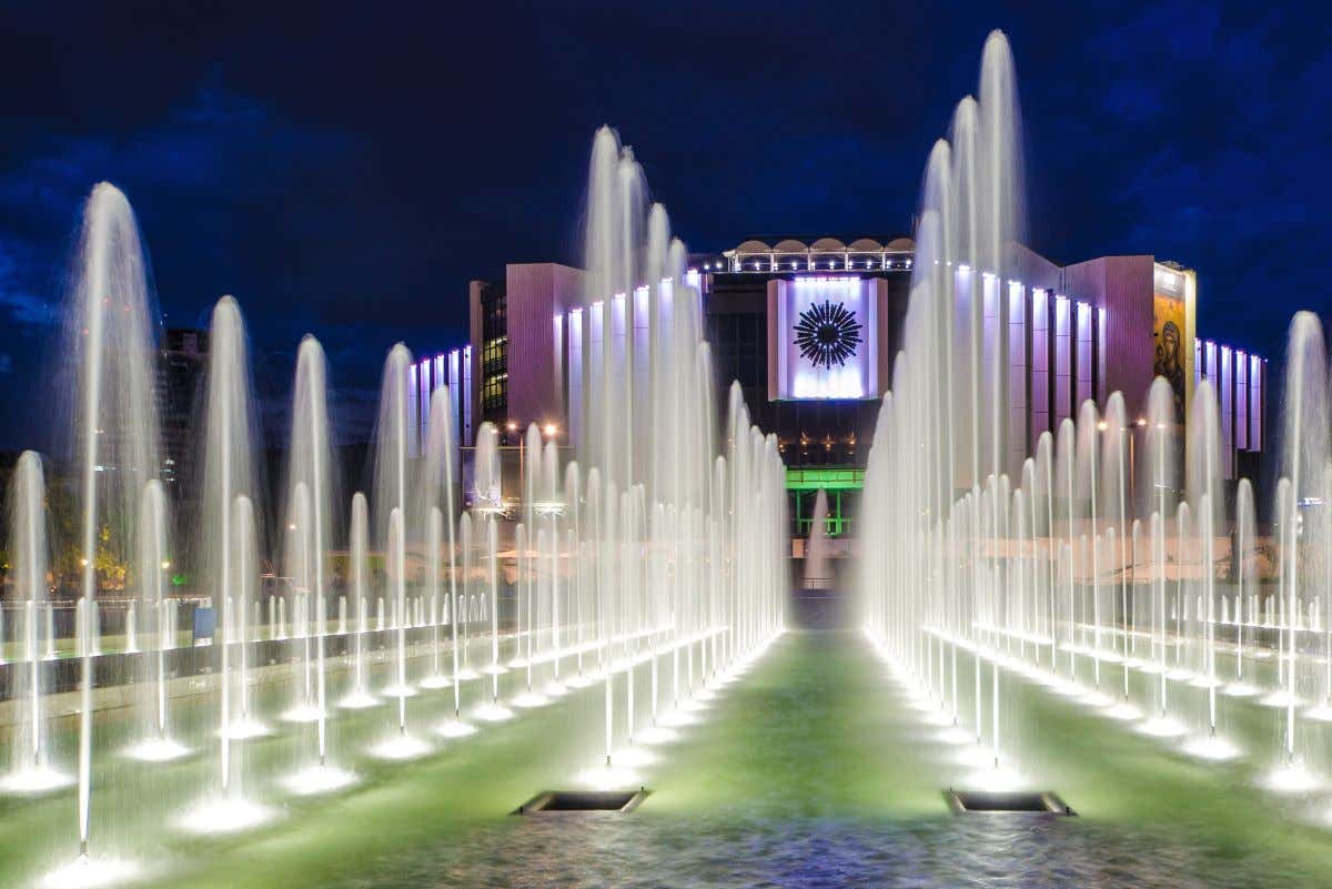 Unas fuentes iluminadas por la noche frente a un palacio