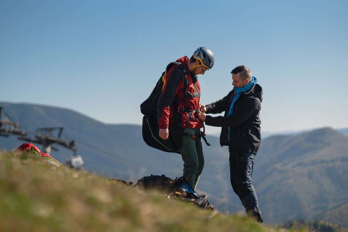 Dos hombres preparan arneses y cascos en lo alto de una montaña