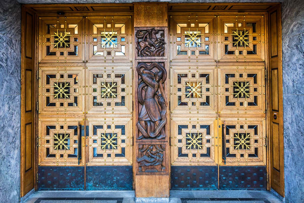 Una puerta de madera muy decorada, con esculturas y vidrios, perteneciente al ayuntamiento de Oslo