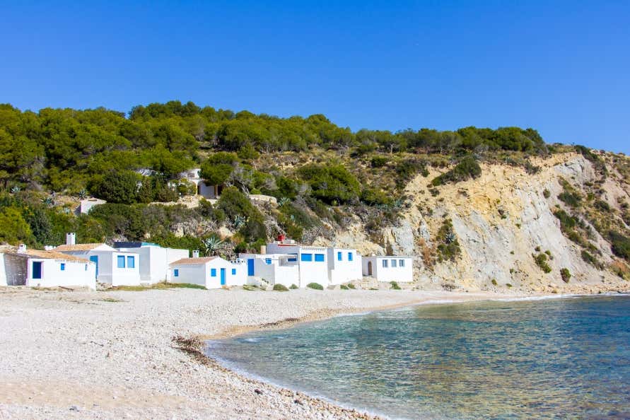 A view of a beach on Portichol Island with white houses with blue doors along the shore, under a blue sky.