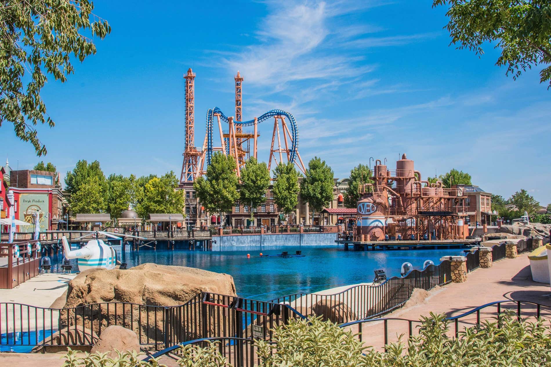 Vista panorámica del Parque Warner Madrid con muchas atracciones, una laguna y el cielo azul de fondo