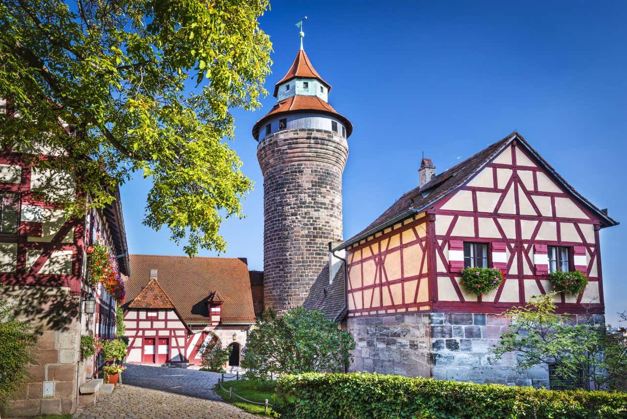 A minaret, part of the Nuremberg castle, next to other medieval-like buildings at the end of an empty cobblestone street on a sunny day