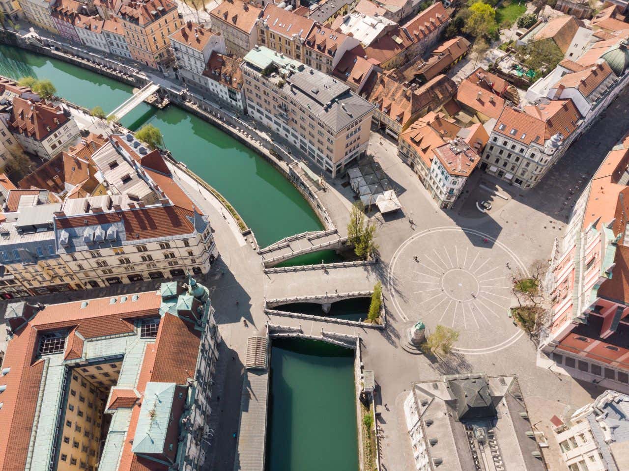 Vista aerea del centro di Lubiana, con i tre ponti che attraversano il fiume e sulla destra una piazza circolare in una giornata di sole