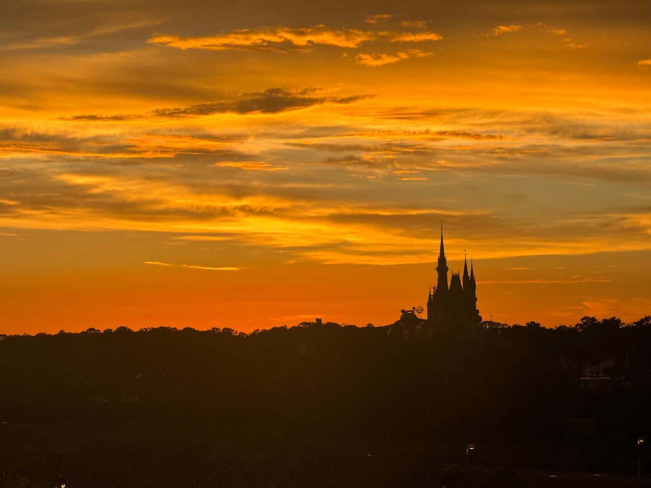 The silhouette Disney castle at Disney World Orlando seen from afar with an orange sky in the background.