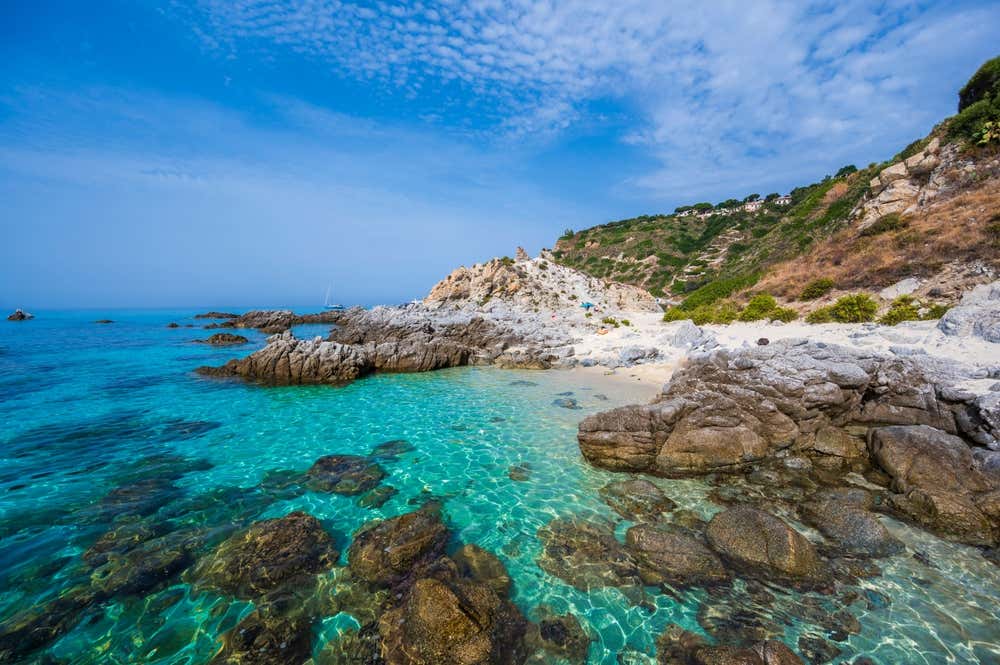 Una piccola spiaggia rocciosa con alcuni bagnanti che prendono il sole sulle rocce e il mare turchese e trasparente della Calabria, a Capo Vaticano