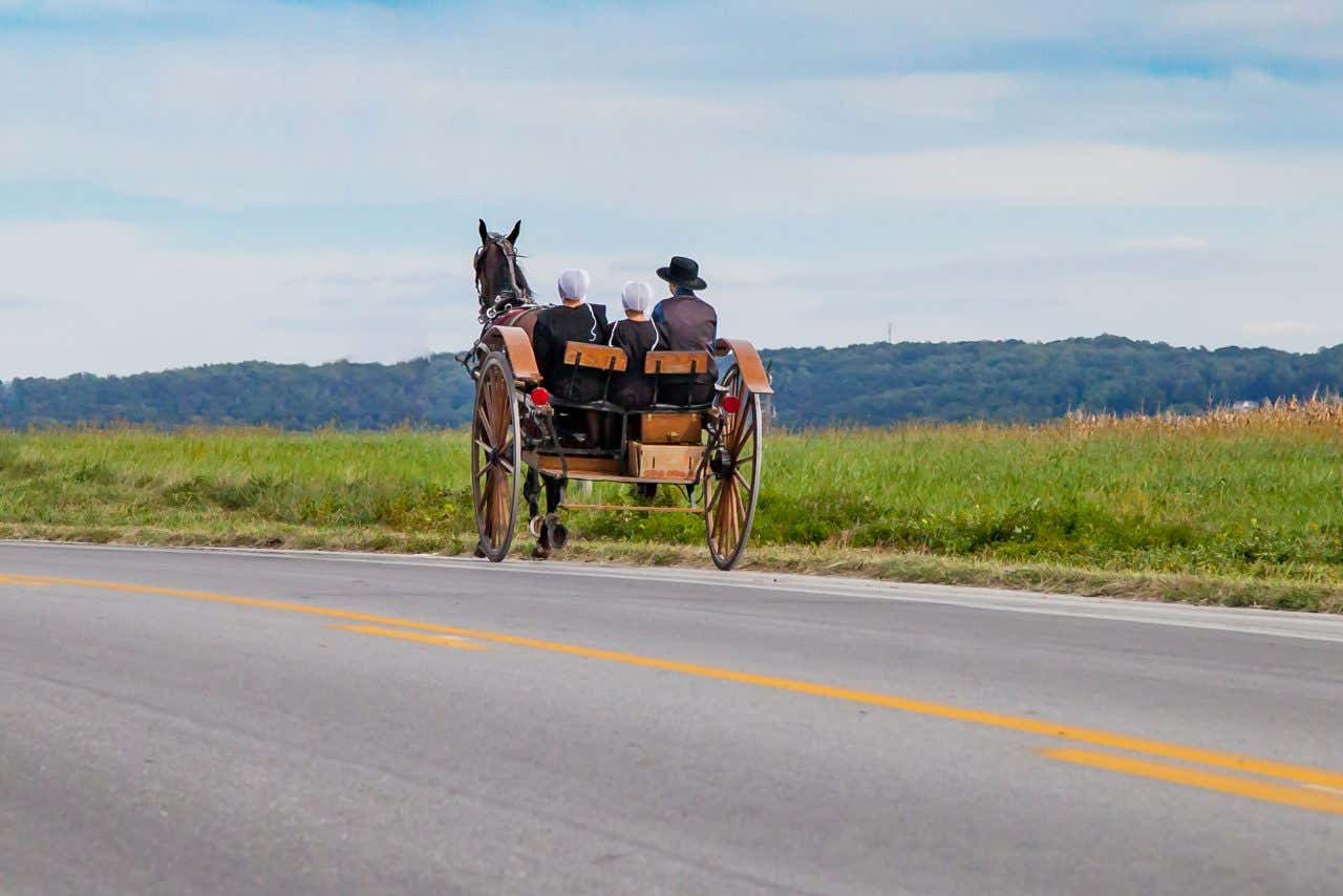 A horse-drawn carriage carrying an Amish family of three rides down an empty paved road in Lancaster, Pennsylvania.