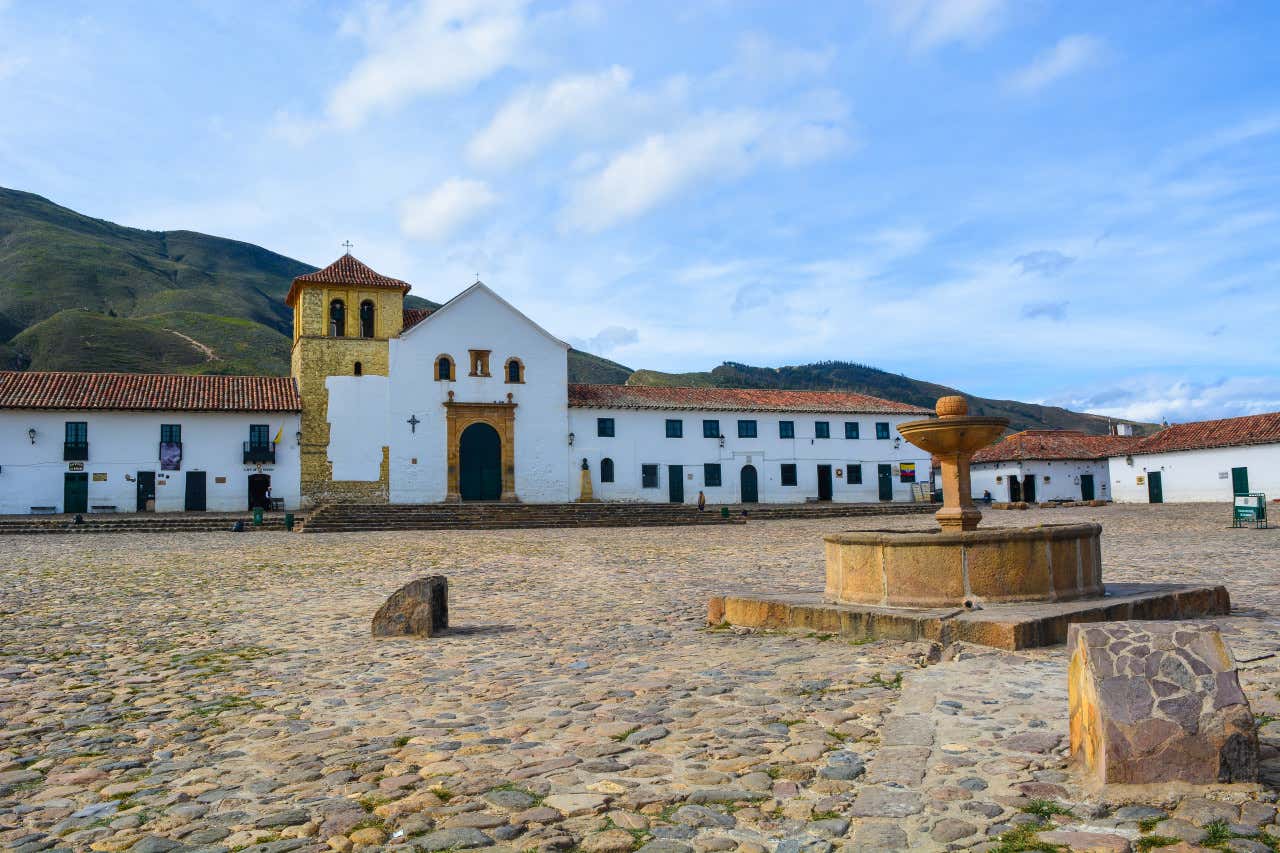 Una fuente de piedra en la mitad de una plaza con casas de estilo colonial a su alrededor