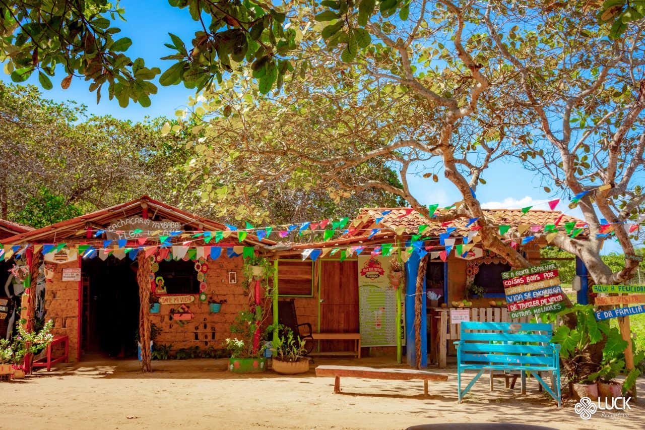 Casinhas de barro em chão de terra decoradas com enfeites coloridos e bandeirinhas