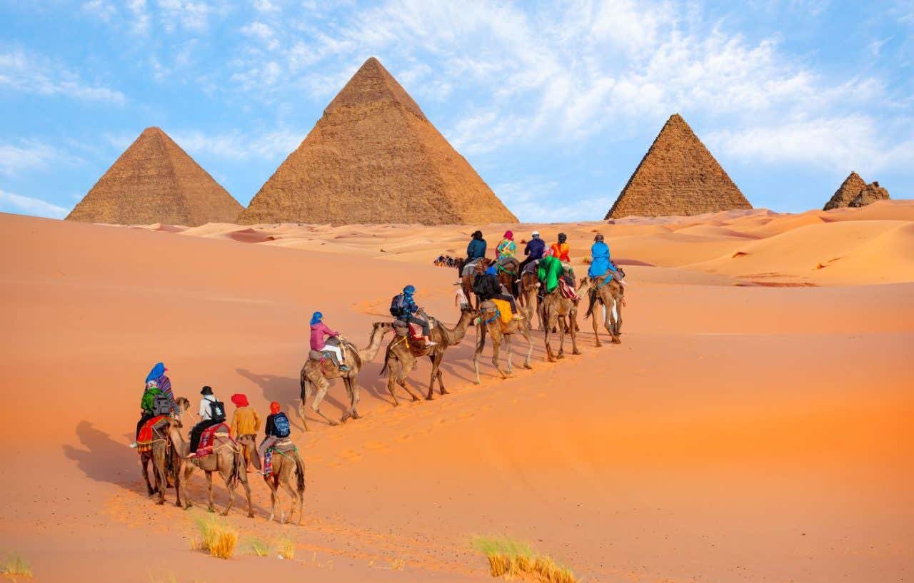 Unas personas en camello en el desierto con las pirámides de Giza al fondo