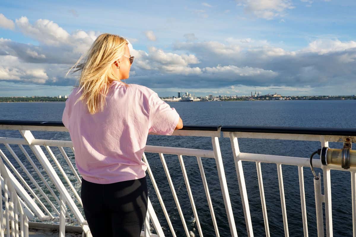 Una mujer rubia de espaldas a la cámara contemplando desde un barco la costa de una ciudad