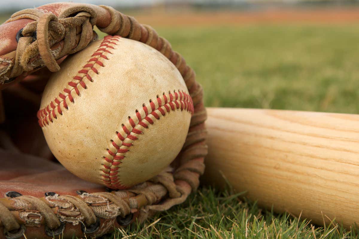Un guante de béisbol en el césped con una pelota y junto a un bate