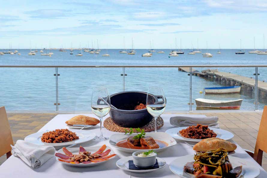 Diferentes platos típicos de arroz, salazones y pescado en una mesa a orillas del puerto del Mar Menor