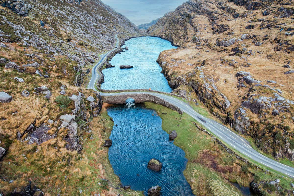 Vista aérea de una carretera entre montañas y atravesando un puente de piedra sobre un lago