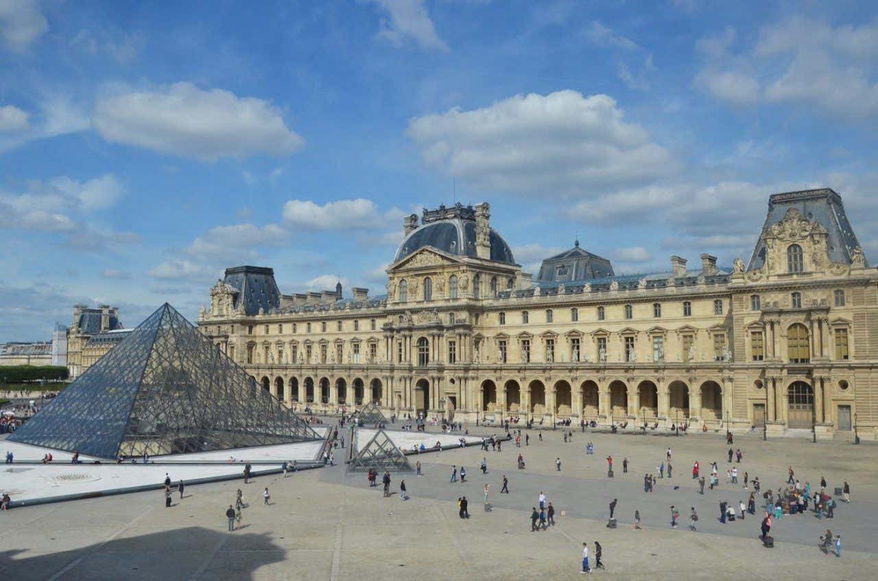 Panorámica del Museo del Louve, donde se aprecia la plaza y varias personas caminando