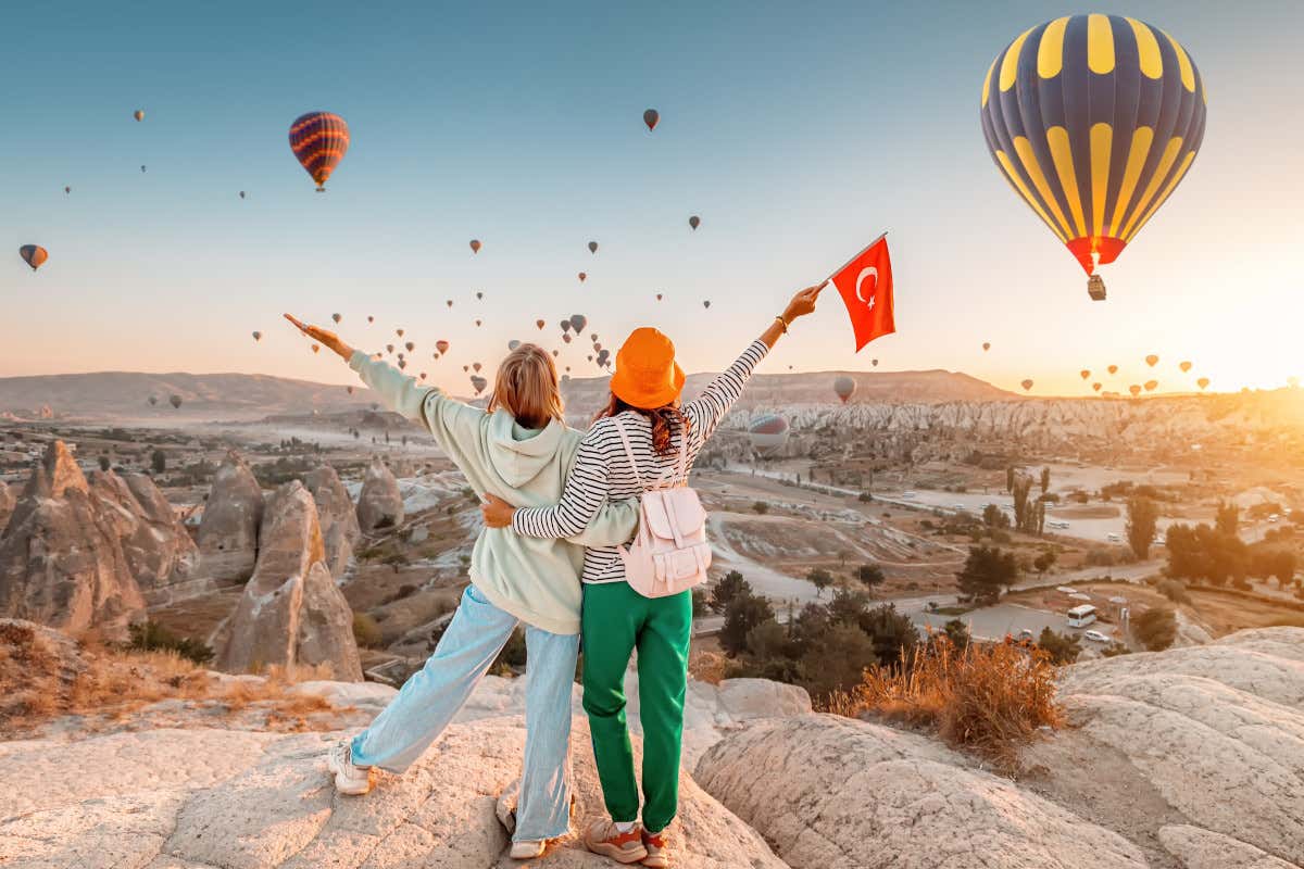Dos mujeres, una de ellas sosteniendo la bandera de Turquía, contemplan varios globos aerostáticos volando sobre las rocas de la Capadocia