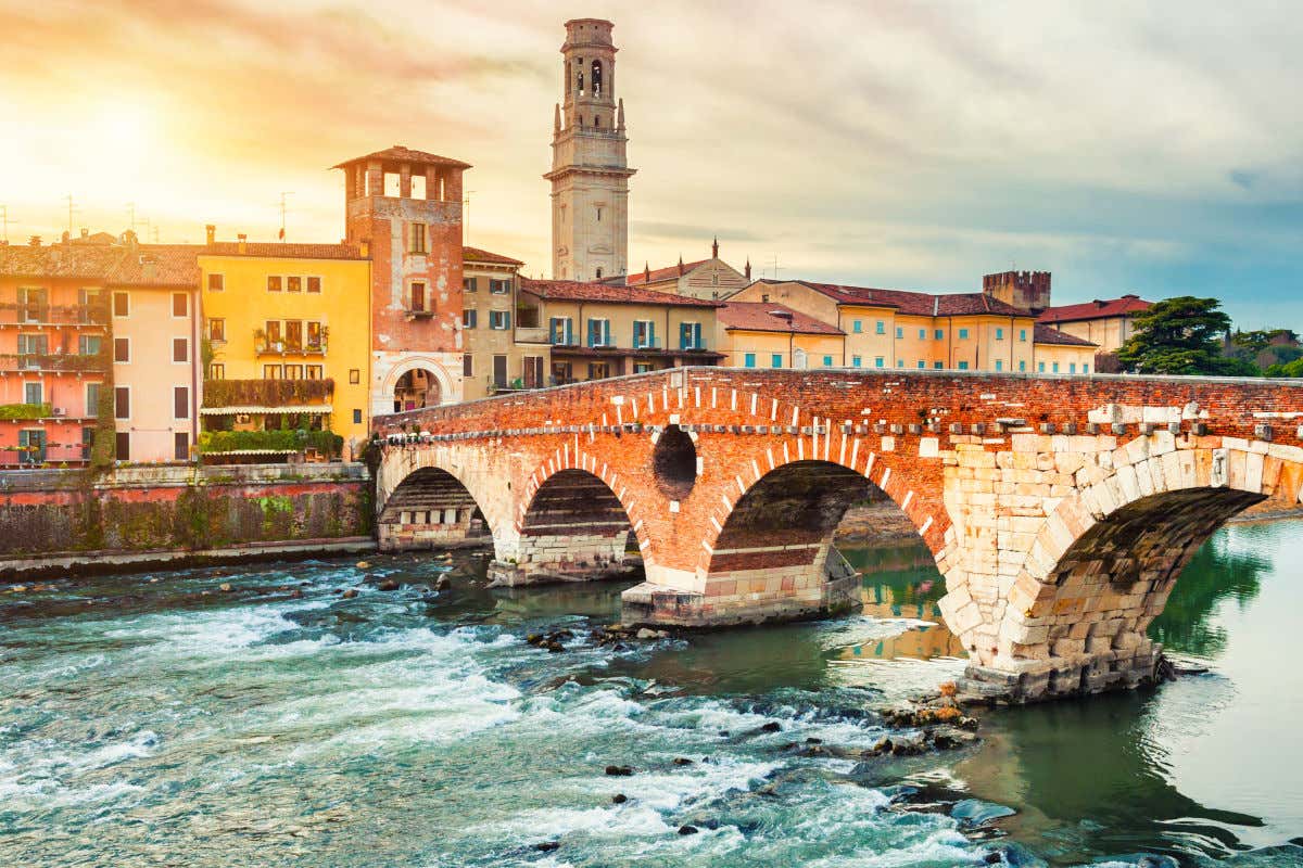 Un antiguo puente de piedra con varios arcos levantado sobre un río y frente a varios edificios en Verona