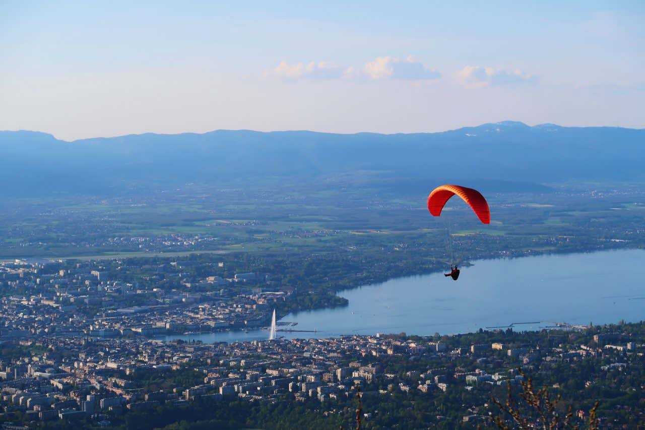 Parapentiste survolant Genève depuis le mont Salève, lac Léman et montagnes en arrière-plan