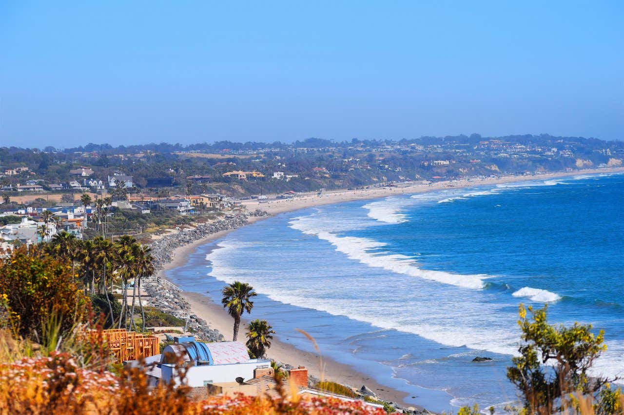 An high-up view of a beach in Malibu at high tide, with lots of buildings along the coast.