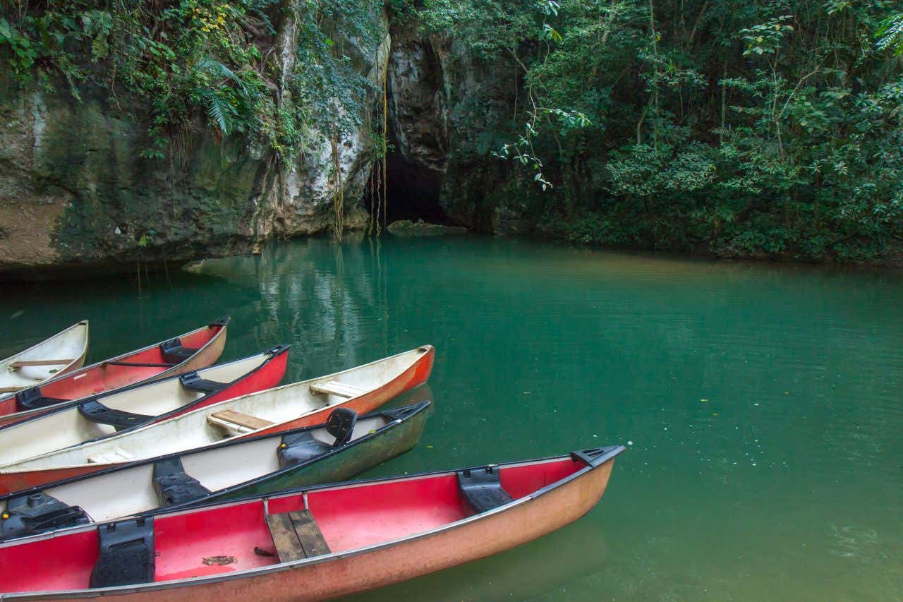6 empty canoes sitting on the water near a dark cave in Barton Creek.
